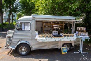 Ein alter Foodtruck, der in einem sonnigen Bereich im Freien geparkt ist, stellt Gläser, Flaschen und verpackte Lebensmittel auf Regalen und einem Tisch aus - perfekt, um die DANKE-Spezialitäten von 2023 zu entdecken.