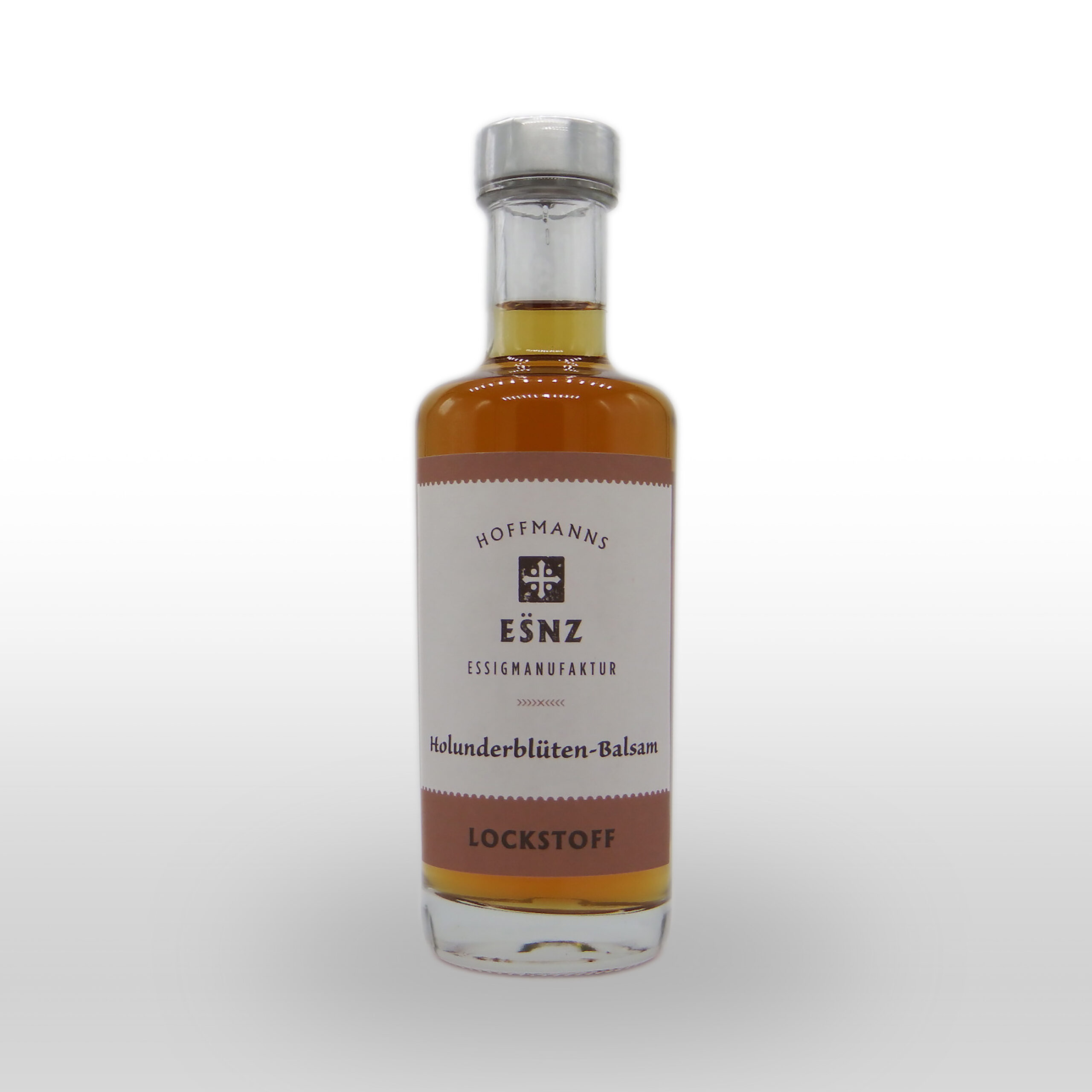 Eine mit bernsteinfarbenem Holunderblüten-Balsamessig gefüllte Klarglasflasche mit der Aufschrift "Hoffmanns Essigmanufaktur Holunderblüten-Balsam Lockstoff" auf weißem Grund.