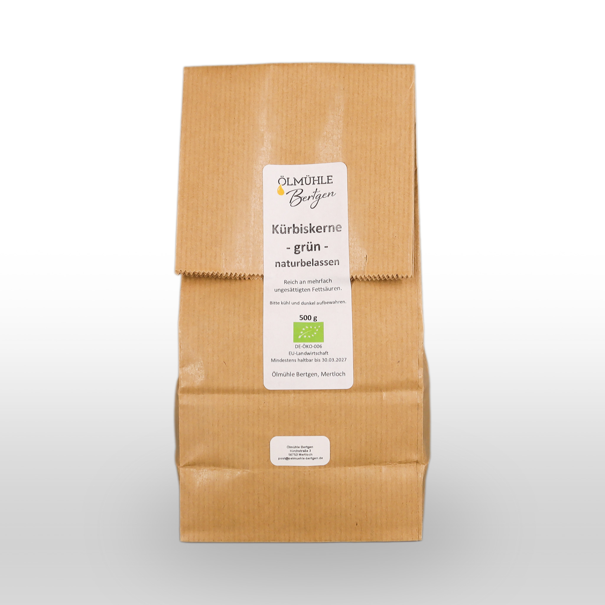 Eine braune Papiertüte mit der Aufschrift "Kürbiskerne - grün - naturbelassen" von der Ölmühle Berghen, die 500 g natürliche grüne Kürbiskerne enthält.